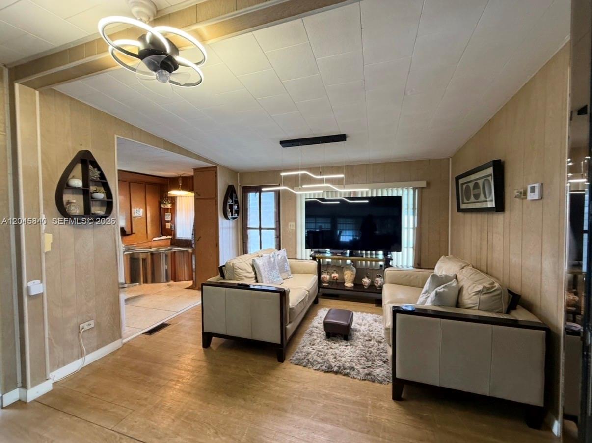 A living room features wood-paneled walls, two beige sofas, a shag rug, and modern lighting — 3309 Orange ST, Hollywood FL 33021, HOLLYWOOD, FL