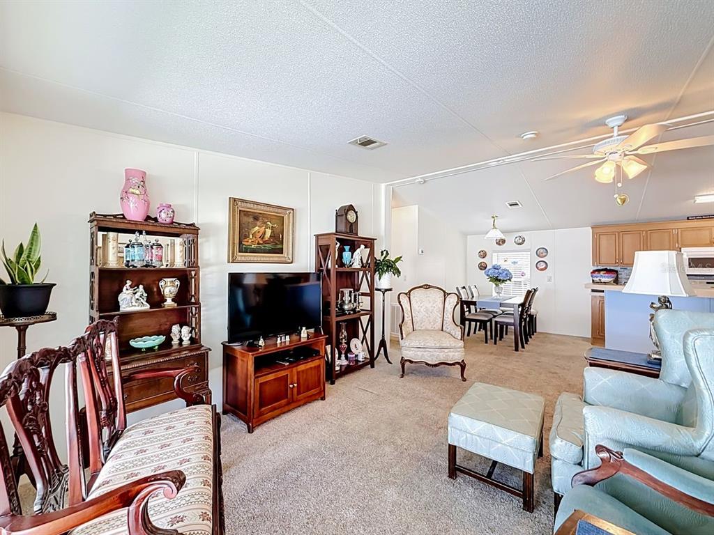 A living room with carpeted floors, wooden furniture, and an adjacent dining area and kitchen — 1660 ELKHART CIRCLE, TAVARES, FL