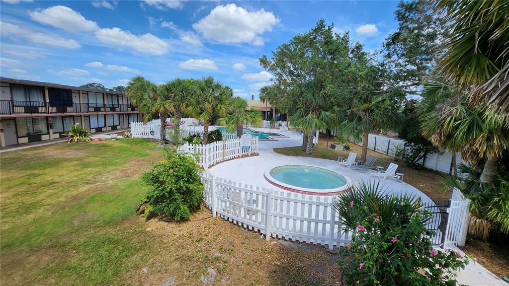 An outdoor pool area with a hot tub, white fencing, and palm trees near a building — 7900 S ORANGE BLOSSOM TRAIL UNIT 2102, ORLANDO, FL
