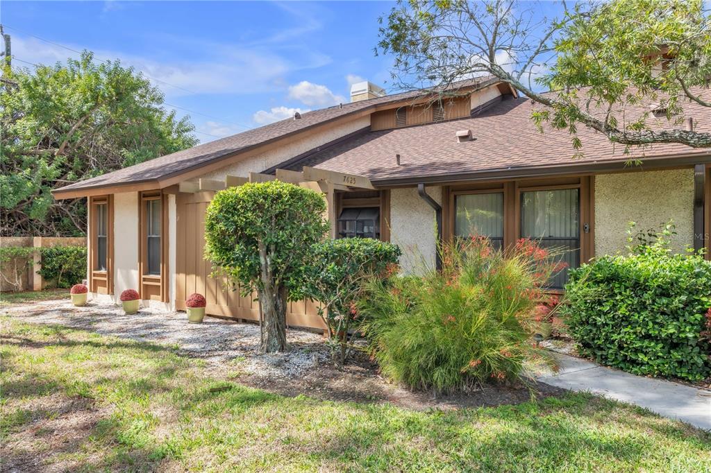A single-story house with a brown shingled roof, stucco walls, and a wooden pergola entrance — 7625 4TH AVENUE W UNIT 7625, BRADENTON, FL
