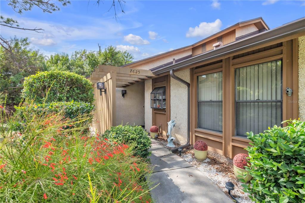 A walkway leads to the front entrance of a house with a wooden pergola — 7625 4TH AVENUE W UNIT 7625, BRADENTON, FL