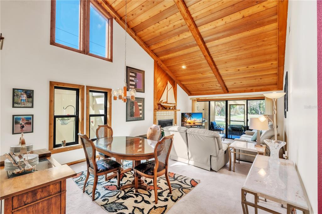 A dining area and living room with a vaulted wood-paneled ceiling and sliding glass doors — 7625 4TH AVENUE W UNIT 7625, BRADENTON, FL