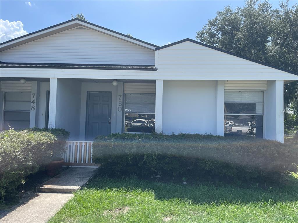 A single-story duplex with white siding, a gray front door, and a manicured hedge — 750 ZELLA LANE, LAKELAND, FL