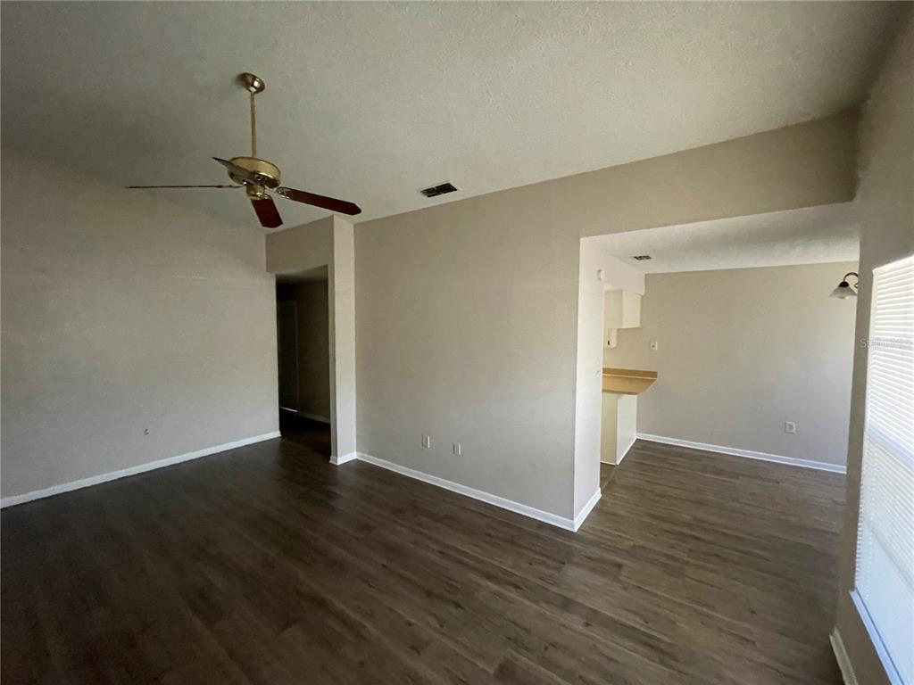 A living room with wood-look flooring, a ceiling fan, and an opening to a kitchen — 750 ZELLA LANE, LAKELAND, FL