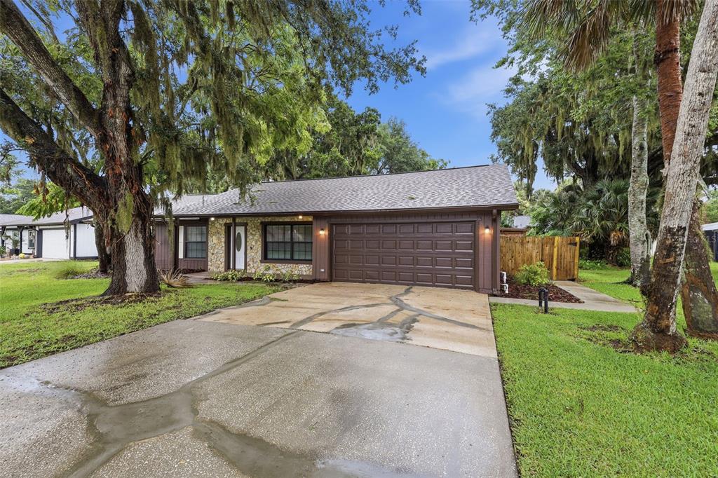 A single-story house with a brown garage, stone facade, and large trees in the yard — 483 SPRUCEVIEW DRIVE, PORT ORANGE, FL