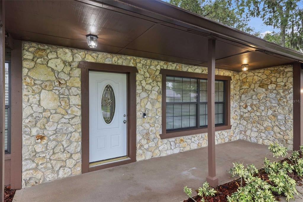 A covered porch with stone walls, a white front door, and dark brown trim — 483 SPRUCEVIEW DRIVE, PORT ORANGE, FL