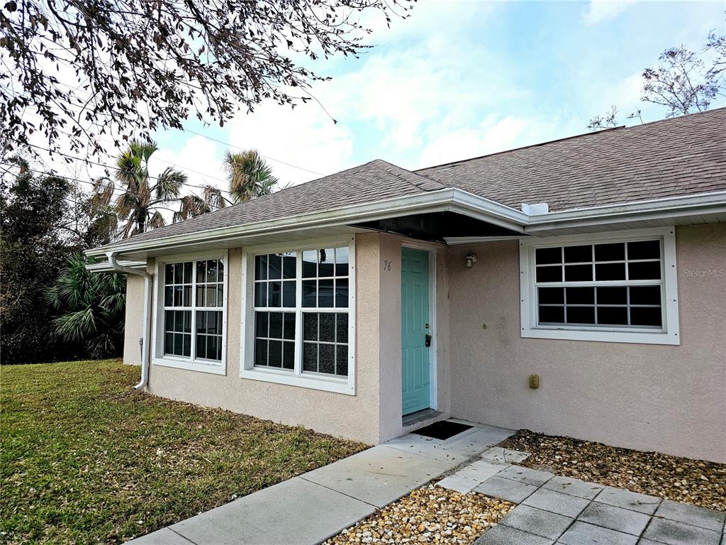 The exterior of a single-story house features a light-colored stucco facade and a teal door — 70 N MCCALL ROAD, ENGLEWOOD, FL