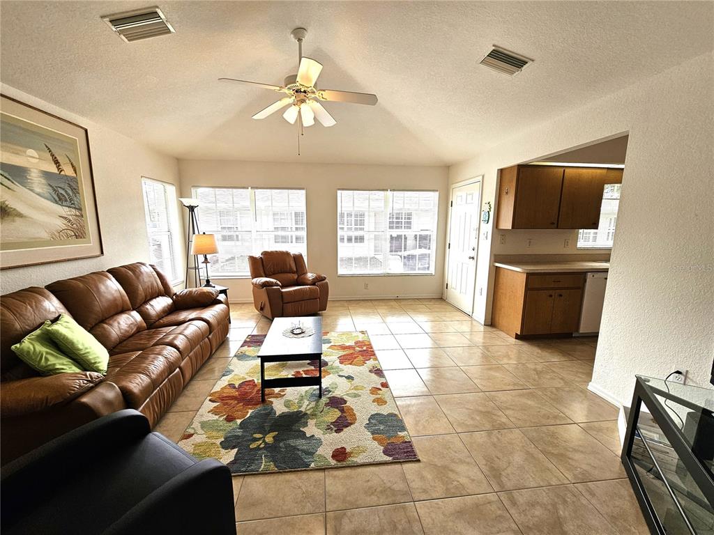 A living room with tile floors, a leather sofa, a floral rug, and an adjacent kitchen — 70 N MCCALL ROAD, ENGLEWOOD, FL