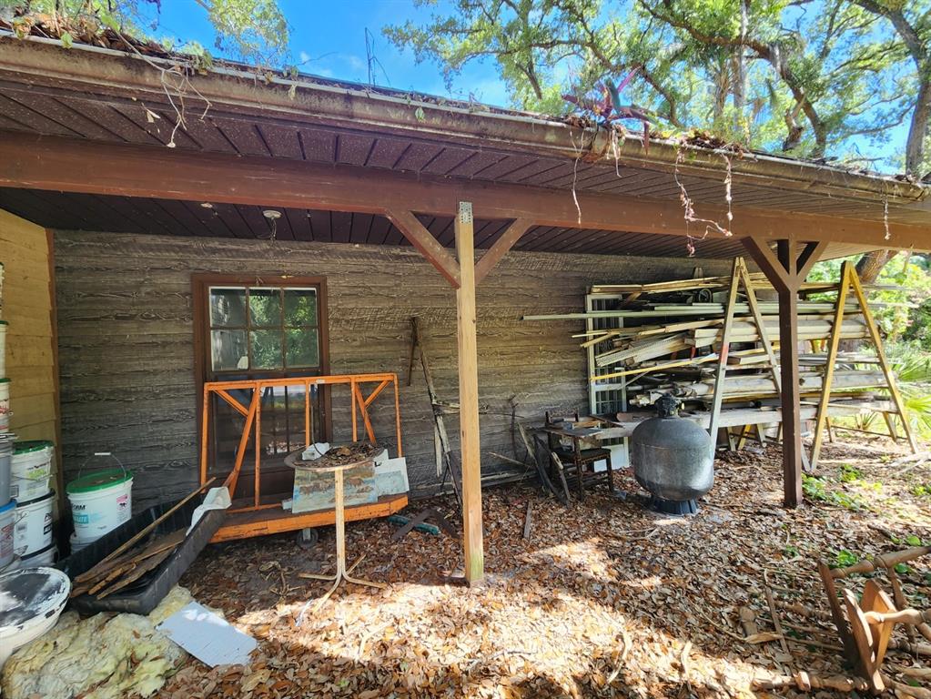 An exterior view of a covered porch with wood siding, a window, and stored equipment — SHAMROCK DRIVE, VENICE, FL