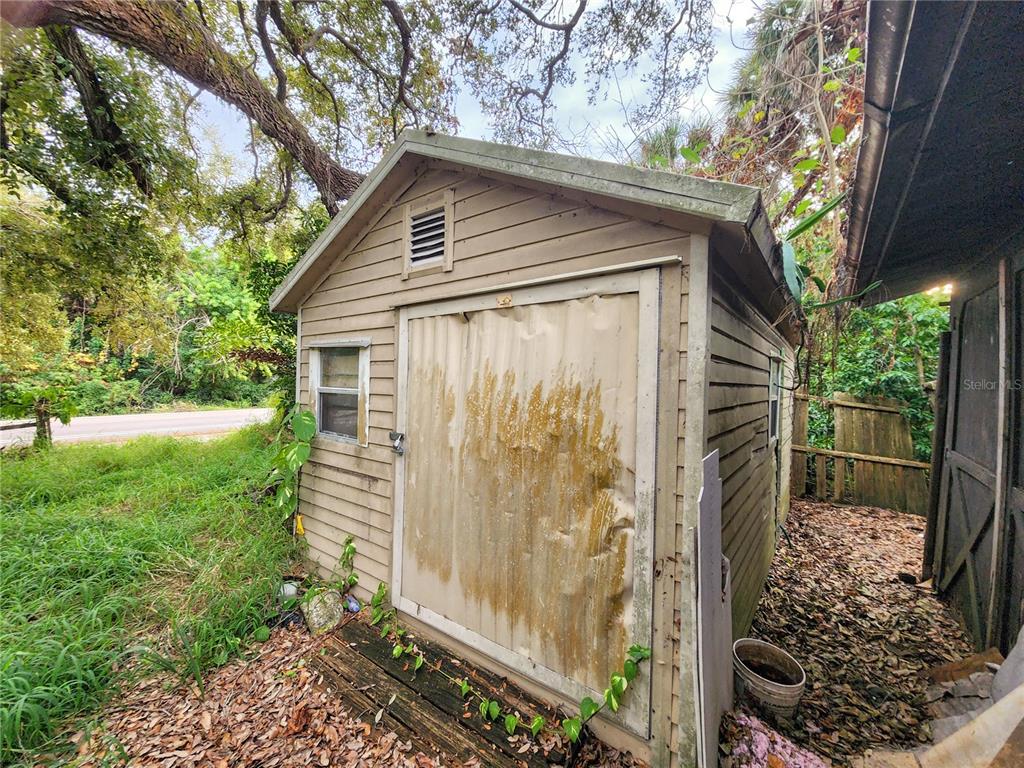 A weathered wooden storage shed sits outdoors next to a fence and overgrown vegetation — SHAMROCK DRIVE, VENICE, FL