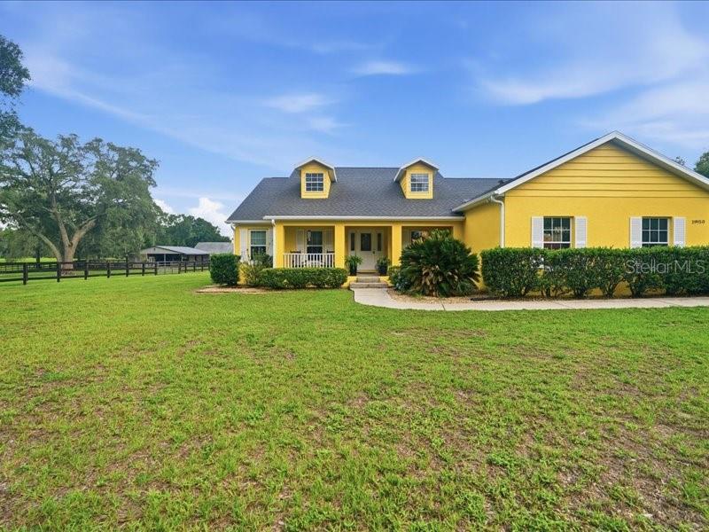 A yellow house with a covered porch and two dormer windows sits on a lawn — 19950 SW 5TH PLACE, DUNNELLON, FL