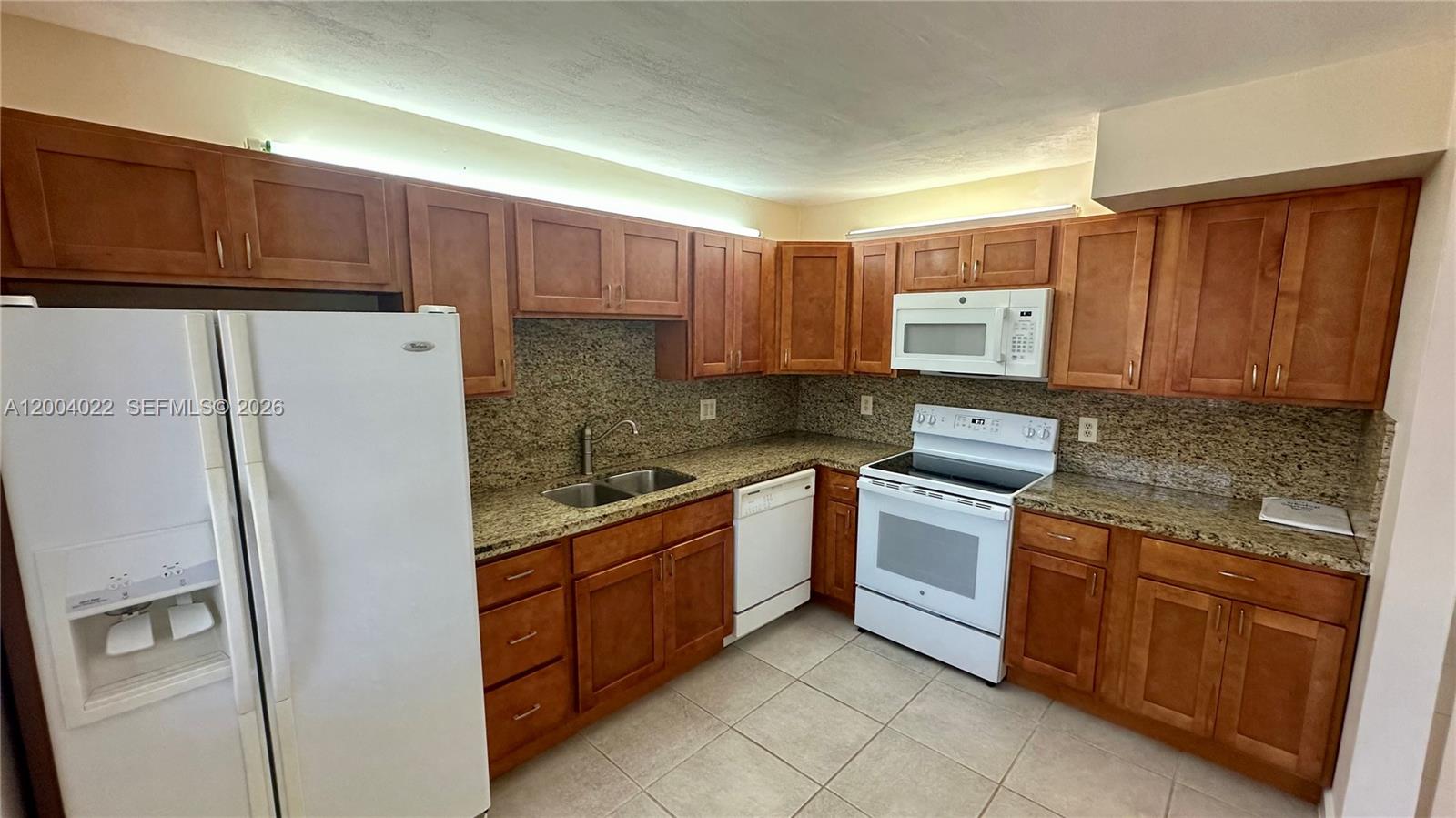 A kitchen features wood cabinets, granite countertops, and white appliances — 16210 Laurel Dr # 203, Weston FL 33326, WESTON, FL