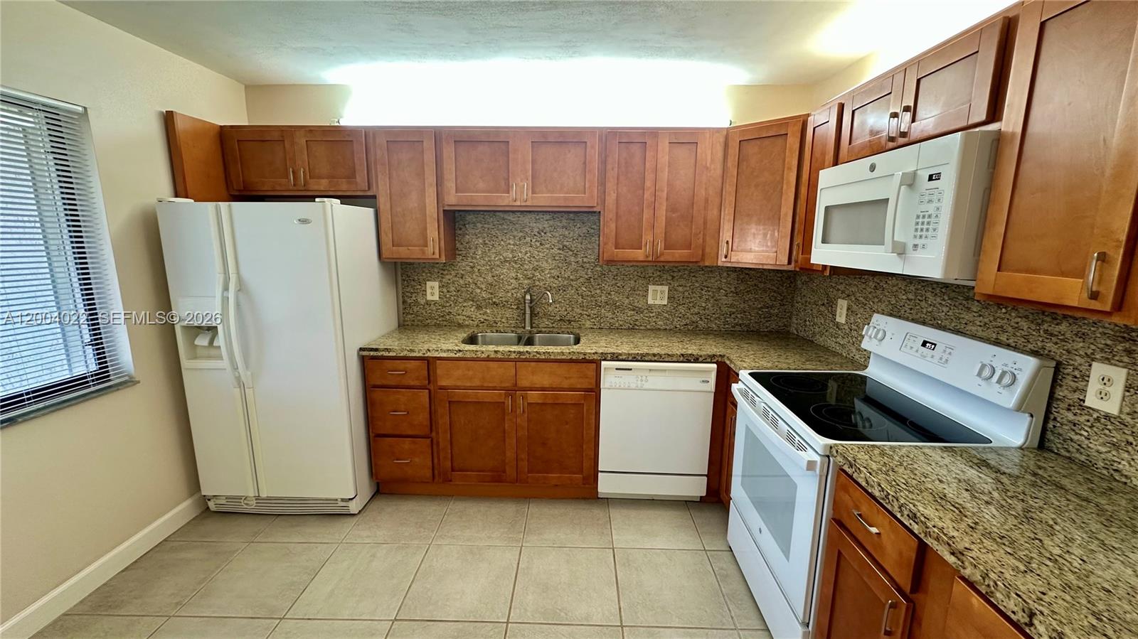 A kitchen features wood cabinets, granite countertops, tile flooring, and white appliances — 16210 Laurel Dr # 203, Weston FL 33326, WESTON, FL