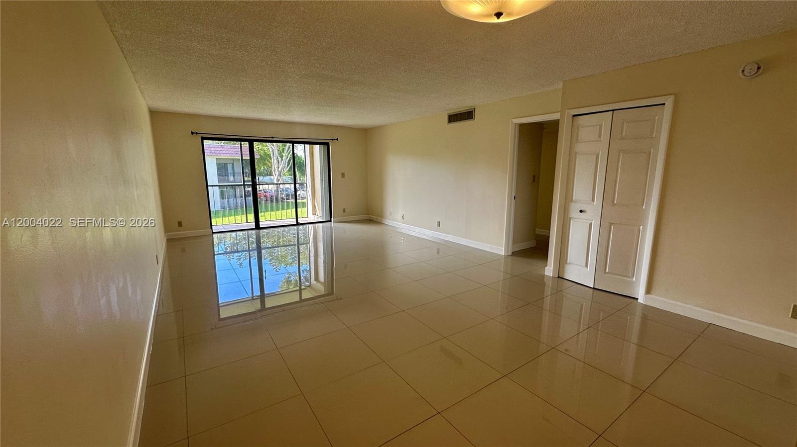 An empty living room features beige tile flooring, light-colored walls, and a sliding glass door — 16210 Laurel Dr # 203, Weston FL 33326, WESTON, FL