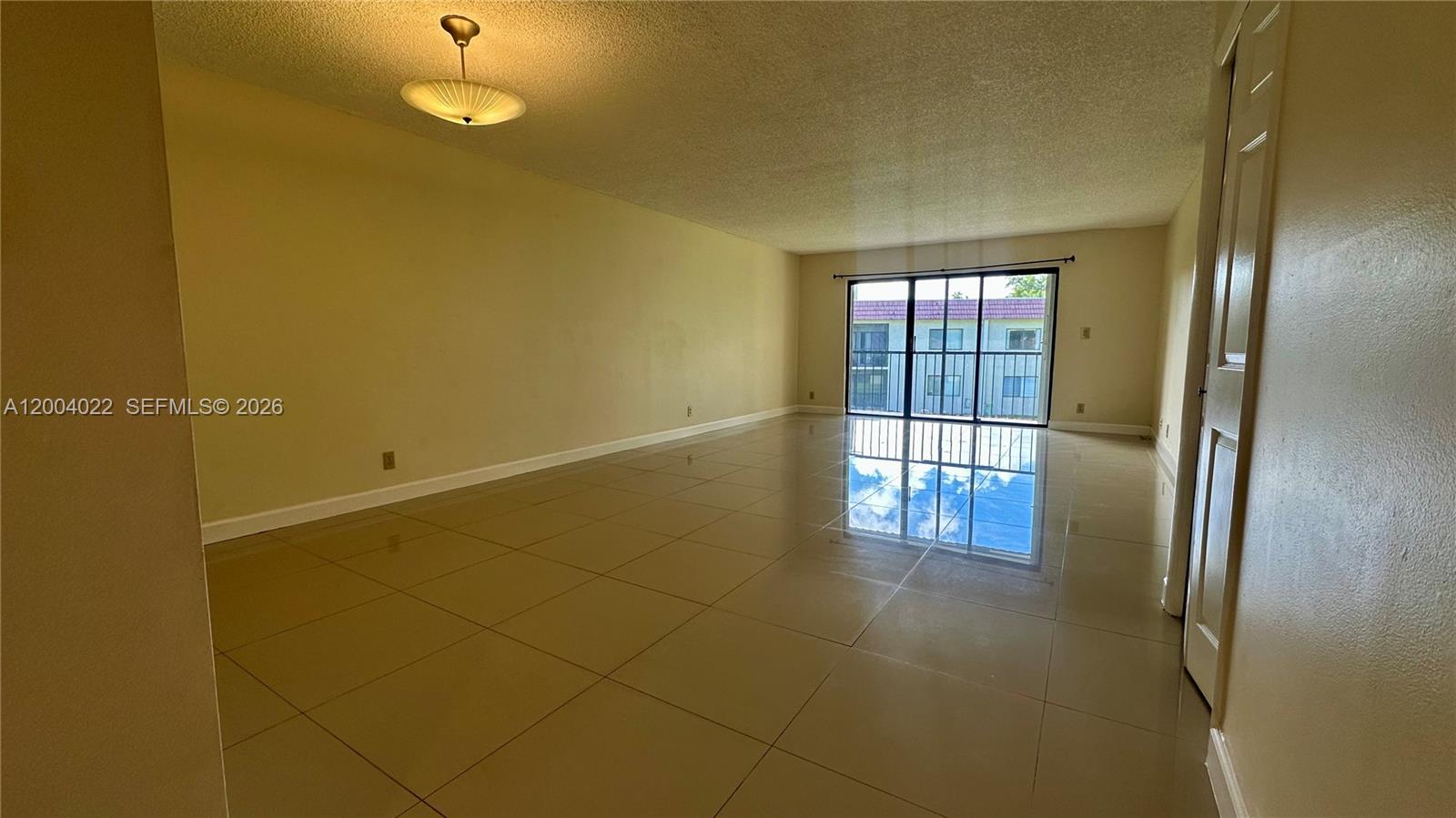 An empty room features beige tiled floors, light-colored walls, and a sliding glass door — 16210 Laurel Dr # 203, Weston FL 33326, WESTON, FL