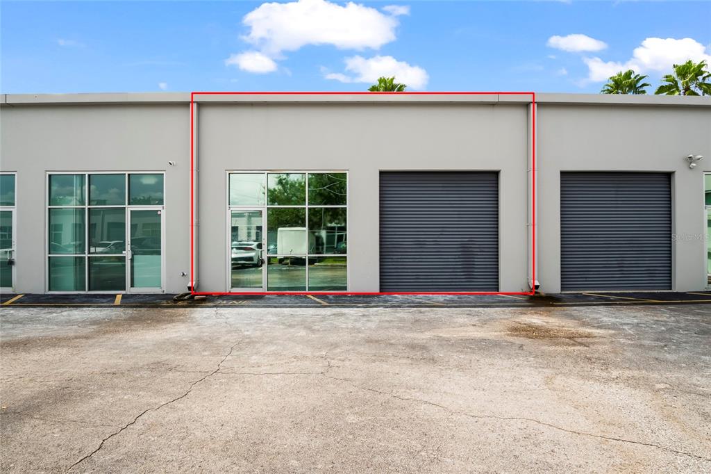 Exterior view of a commercial unit featuring a glass storefront and a roll-up door — 7901 KINGSPOINTE PARKWAY UNIT 2, ORLANDO, FL