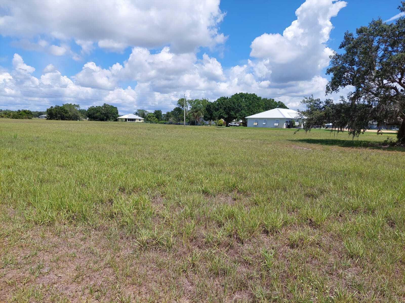 A wide, grassy vacant lot under a blue sky with scattered clouds and distant houses — 7924 Castile Road, Sebring FL 33876, SEBRING, FL