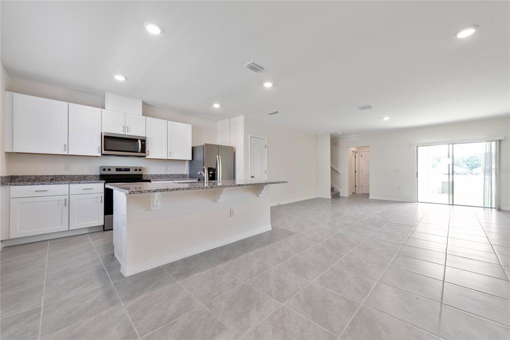 An open-concept kitchen, dining area, and living room feature white cabinets and tile flooring — 1627 BITTEROOT STREET, KISSIMMEE, FL