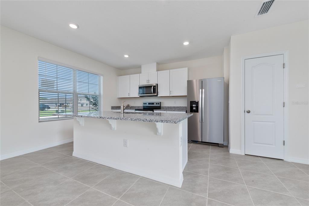A kitchen features white cabinets, granite countertops, a center island, and stainless steel appliances — 1627 BITTEROOT STREET, KISSIMMEE, FL