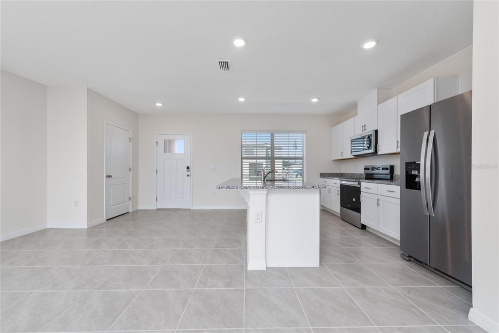 A modern kitchen features white cabinets, granite countertops, stainless steel appliances, and light tile flooring — 1627 BITTEROOT STREET, KISSIMMEE, FL