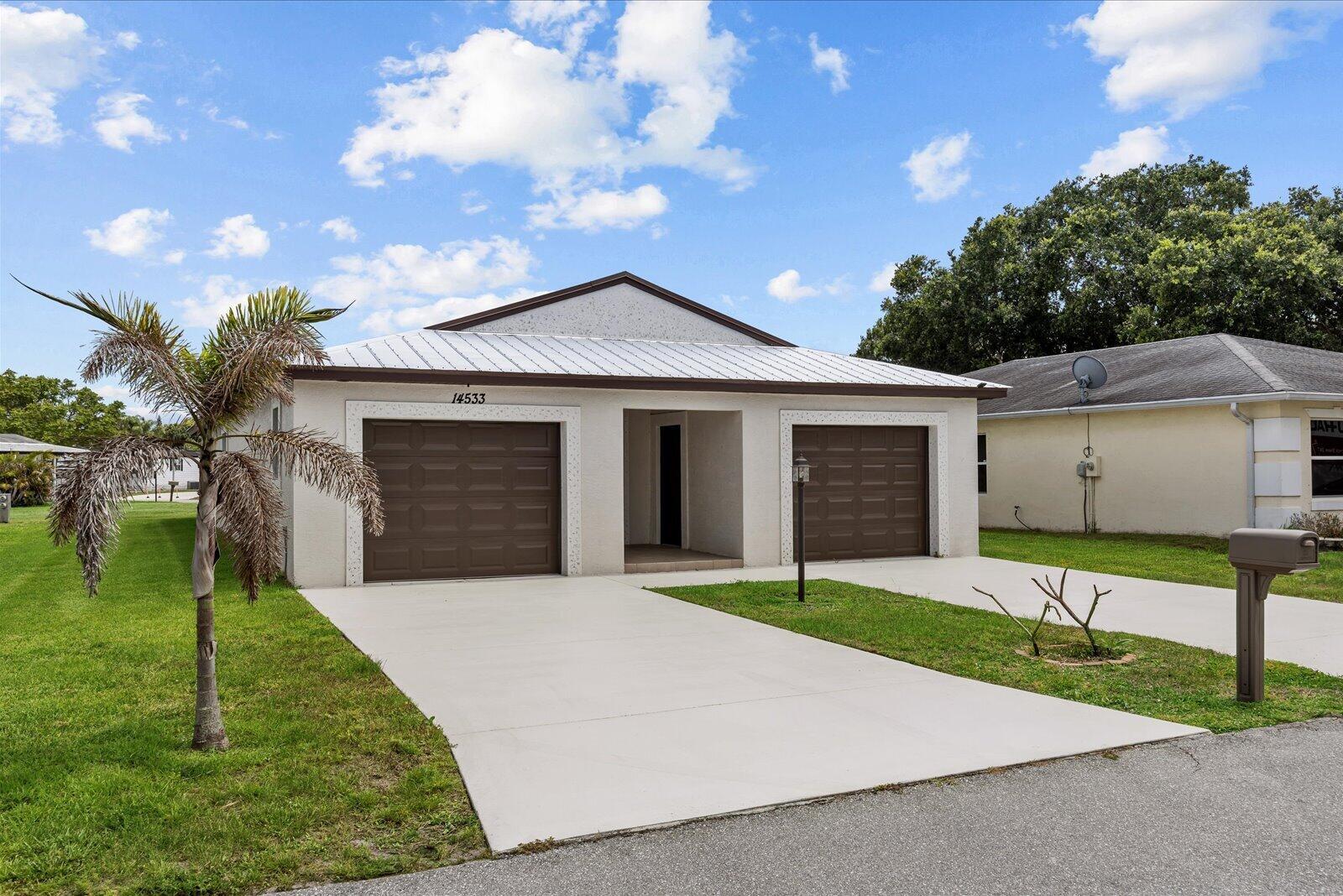 A single-story house with a white stucco exterior, two garage doors, and a metal roof — 14533 Dulce Avenue, Fort Pierce FL 34951, FORT PIERCE, FL