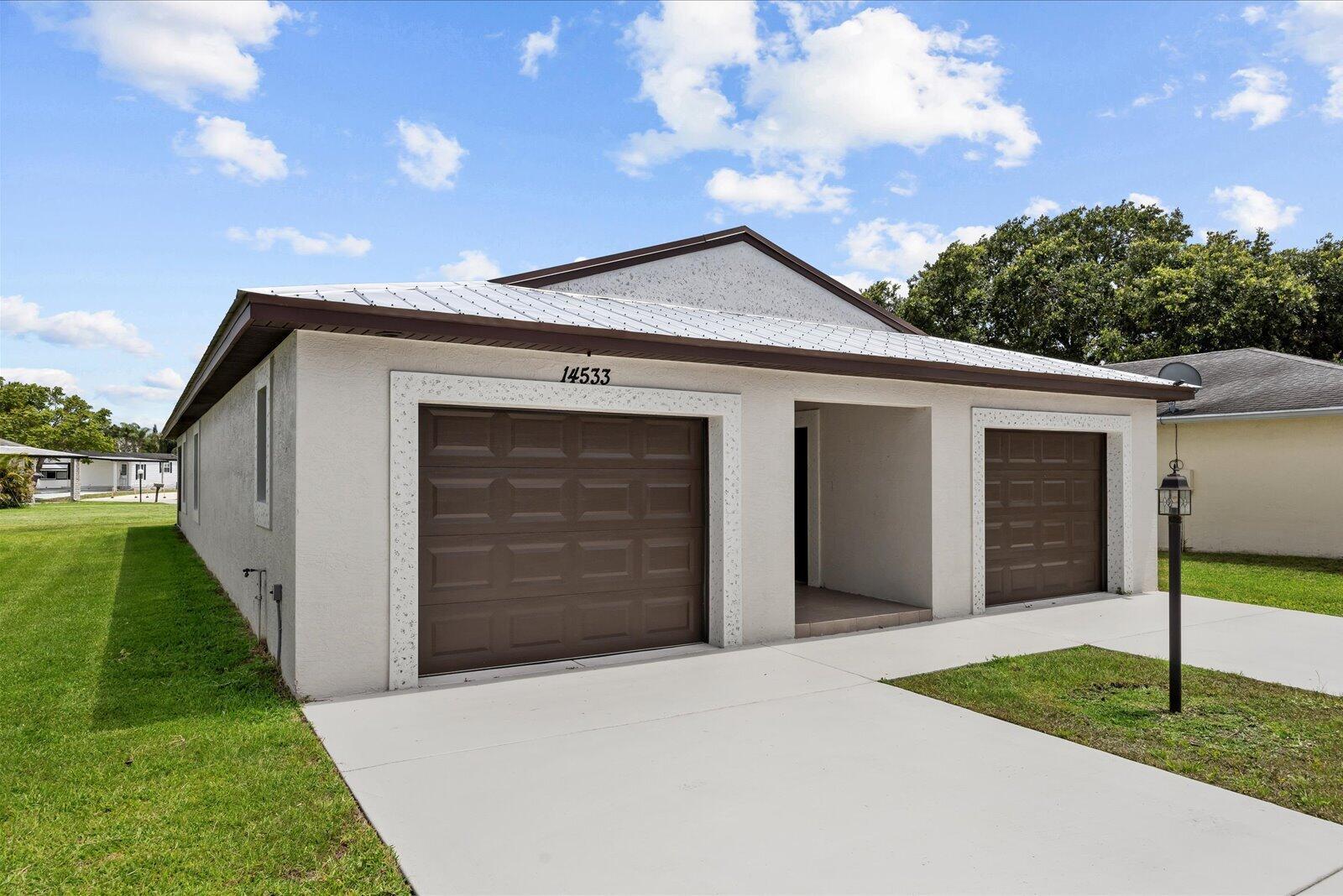 A single-story house features a light-colored stucco exterior, a metal roof, and two garage doors — 14533 Dulce Avenue, Fort Pierce FL 34951, FORT PIERCE, FL
