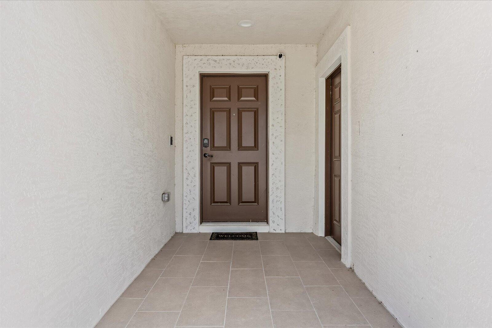 A covered entryway features a brown front door, a side door, and light-colored tile flooring — 14533 Dulce Avenue, Fort Pierce FL 34951, FORT PIERCE, FL
