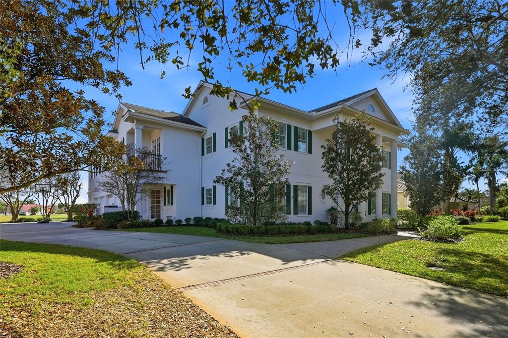 A two-story white house with green shutters and a concrete driveway under a blue sky — 7917 BAYOU CLUB BOULEVARD, SEMINOLE, FL