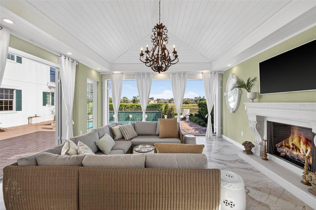 A sunroom features a sectional sofa, a fireplace, and large glass doors opening to a pool — 7917 BAYOU CLUB BOULEVARD, SEMINOLE, FL