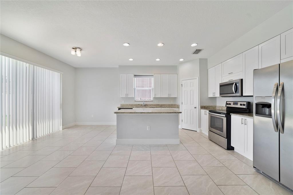 A kitchen features white cabinets, granite countertops, stainless steel appliances, and light-colored tile flooring — 128 WILLOW DRIVE, POINCIANA, FL