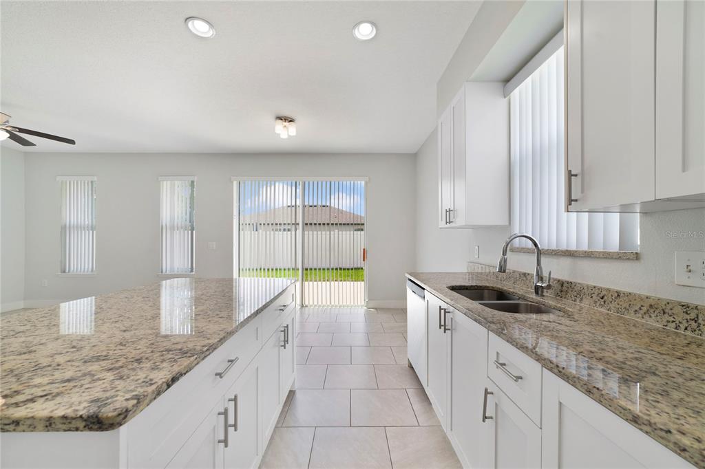 A kitchen with white cabinets, granite countertops, an island, and a sliding glass door — 128 WILLOW DRIVE, POINCIANA, FL
