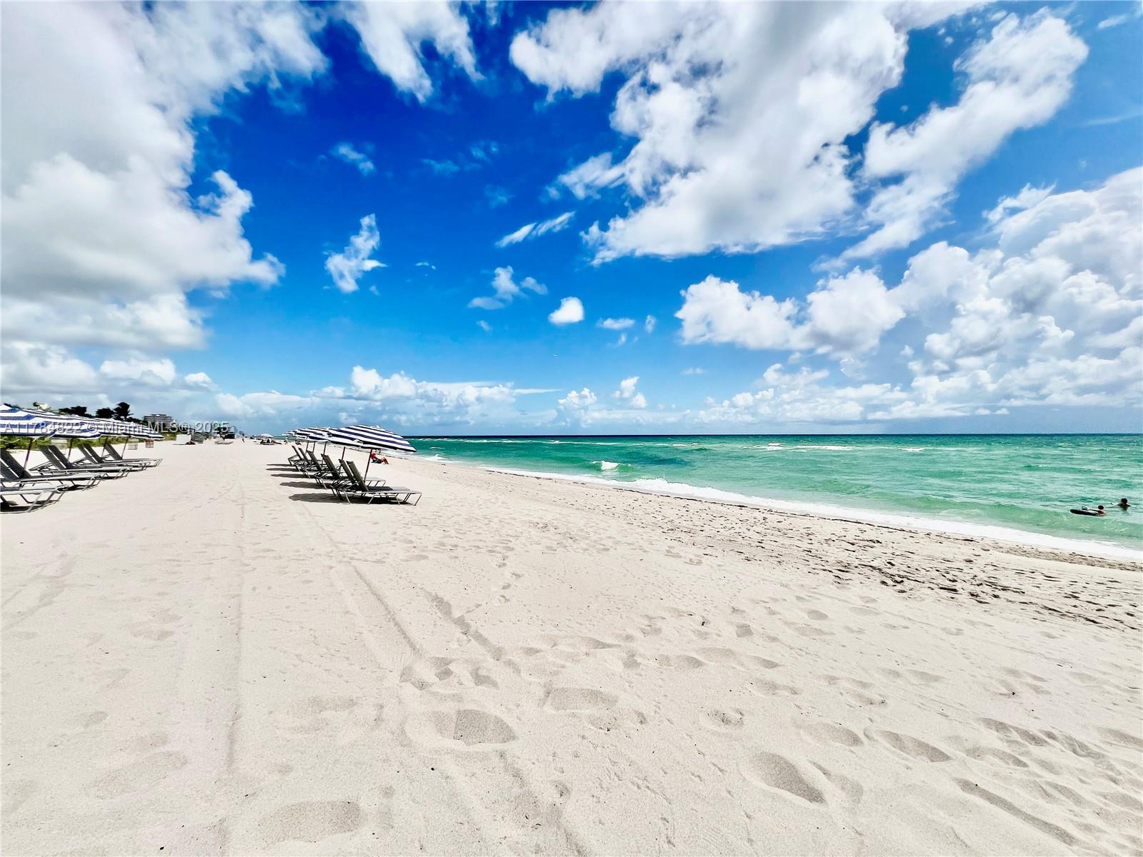 A sandy beach features rows of lounge chairs with umbrellas along the turquoise ocean — 7135 Collins Ave # 621, Miami Beach FL 33141, MIAMI BEACH, FL