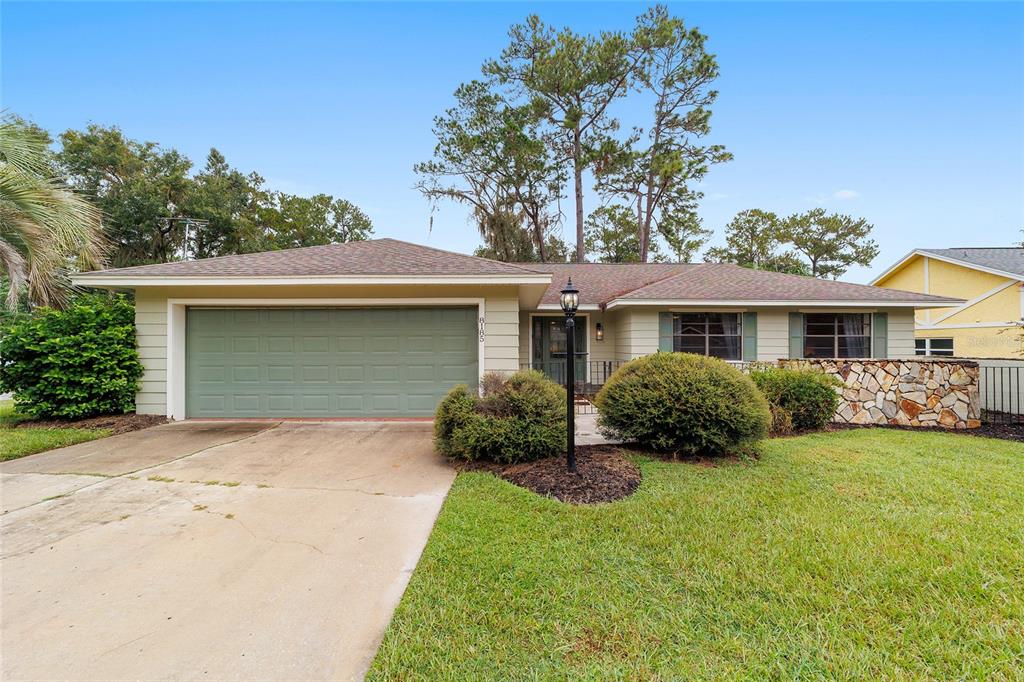 A single-story house with a green garage door, stone facade, and a front lawn — 8185 NW 48TH LANE, OCALA, FL