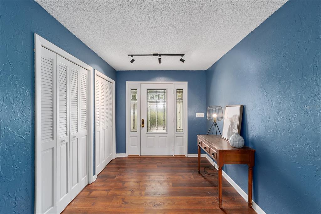 An entryway with blue walls, wood flooring, white louvered closet doors, and a glass-paneled front door — 8185 NW 48TH LANE, OCALA, FL