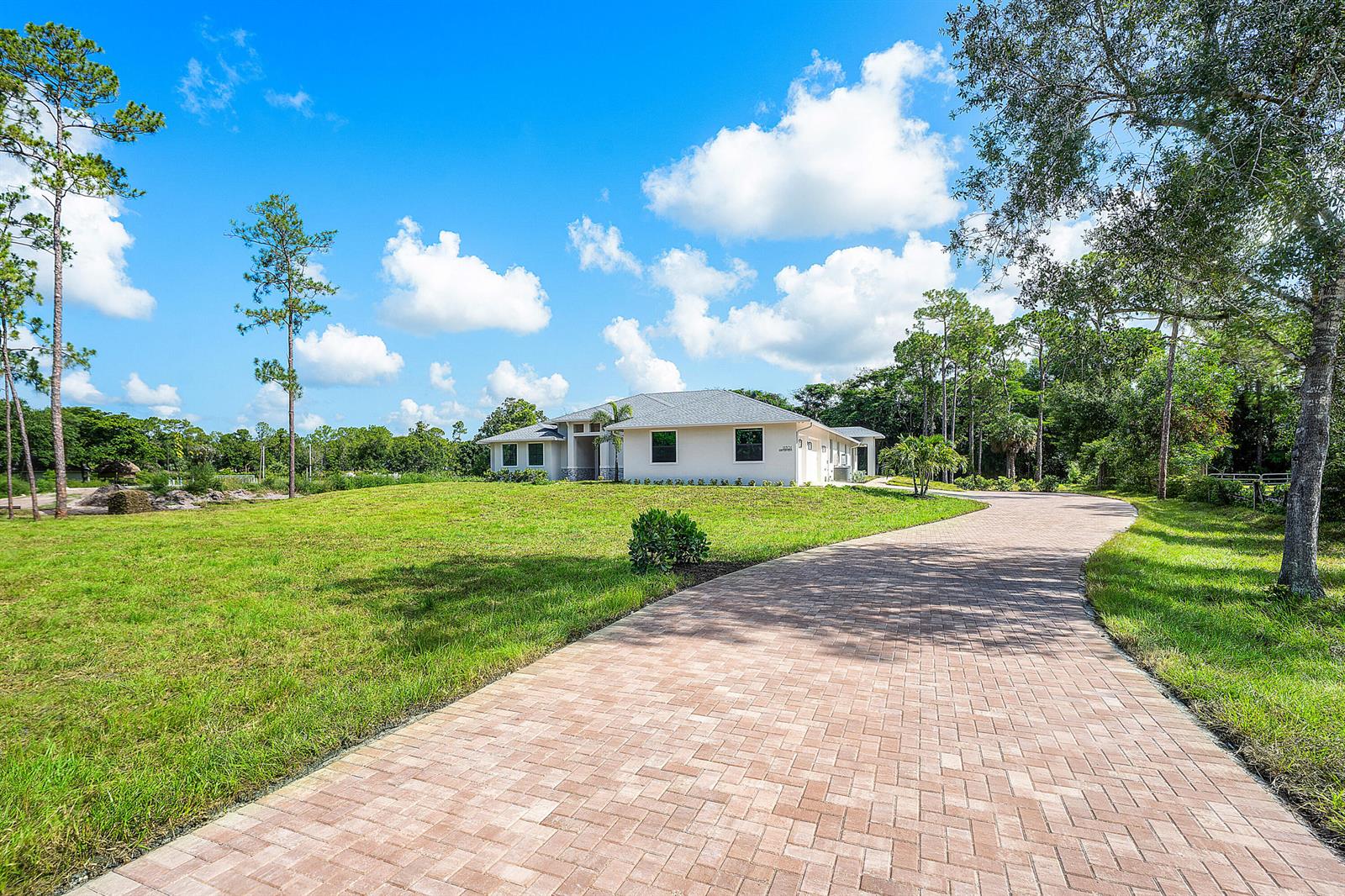 A paved driveway leads to a single-story house surrounded by a grassy lawn and trees — 11701 153rd Court N, Jupiter FL 33478, JUPITER, FL