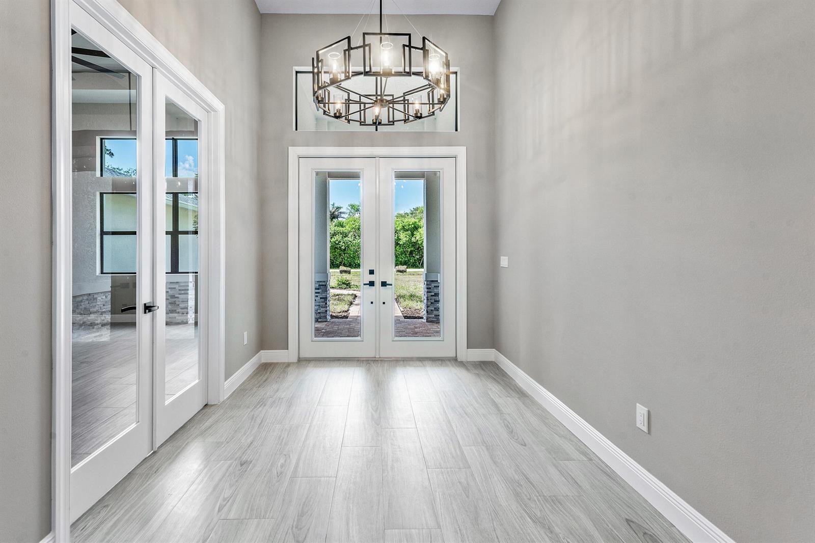 A bright entryway features light wood-look tile flooring, gray walls, and a modern geometric chandelier — 11701 153rd Court N, Jupiter FL 33478, JUPITER, FL