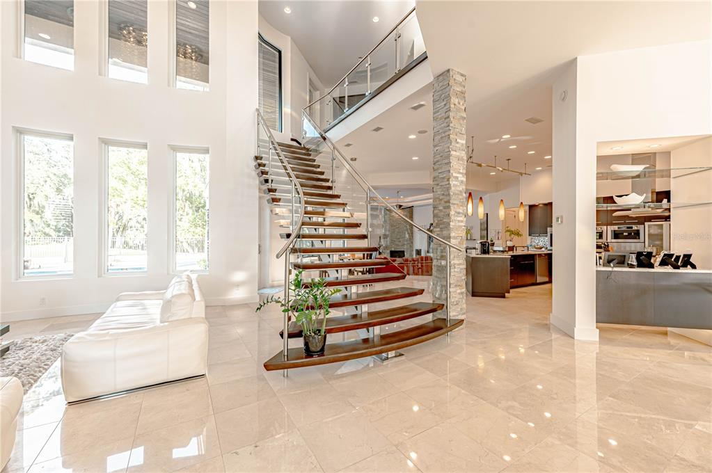 A modern open-concept living area features a curved wooden staircase and polished tile flooring — 410 CANTERWOOD DRIVE, MULBERRY, FL