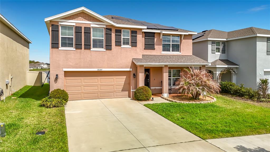 A two-story suburban house with a tan stucco exterior, a two-car garage, and solar panels — 38287 SONNET LANDING AVENUE, ZEPHYRHILLS, FL