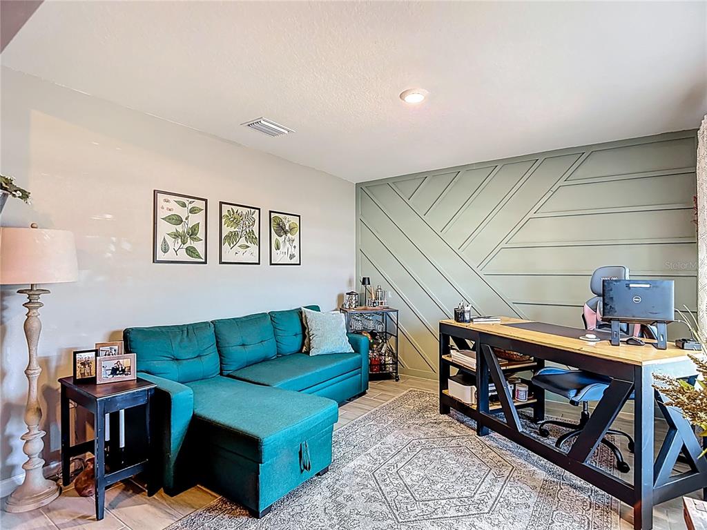 A home office features a teal sectional sofa, a wooden desk, and a green accent wall — 38287 SONNET LANDING AVENUE, ZEPHYRHILLS, FL