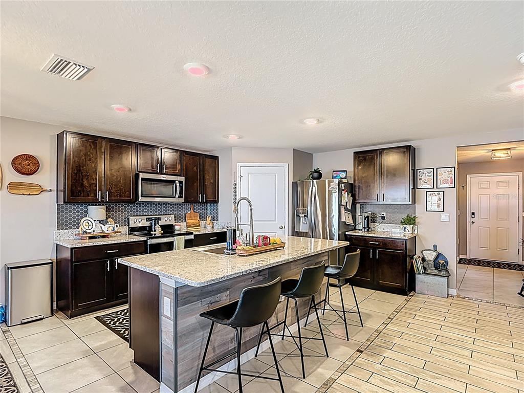A kitchen features dark wood cabinets, granite countertops, a central island, and stainless steel appliances — 38287 SONNET LANDING AVENUE, ZEPHYRHILLS, FL