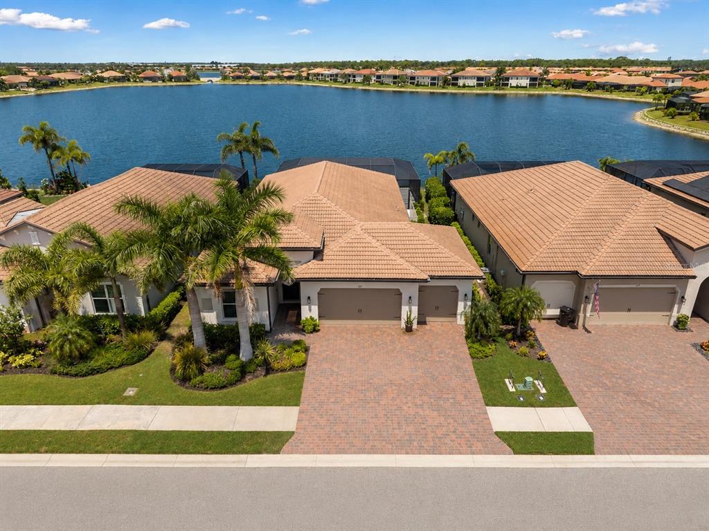 An aerial view shows a suburban house with a tiled roof, garage, and lakefront backyard — 157 VERAZA COURT, NOKOMIS, FL