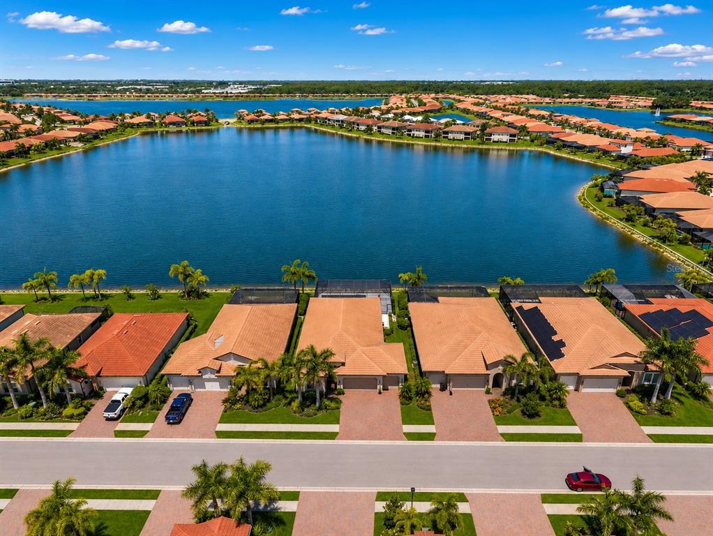An aerial view shows a row of suburban houses with tile roofs bordering a lake — 157 VERAZA COURT, NOKOMIS, FL