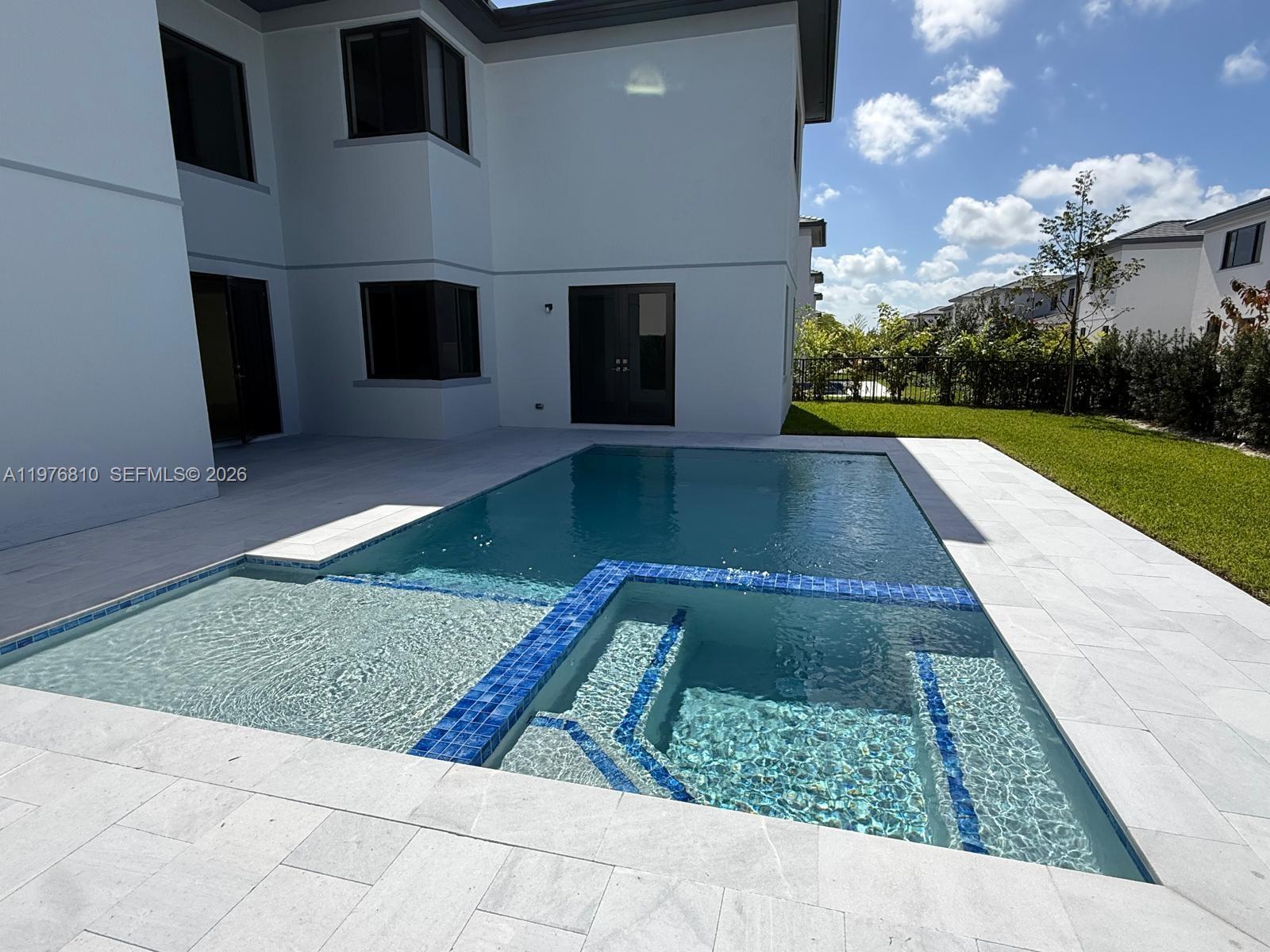 A modern house features a swimming pool with an attached spa and light-colored stone decking — 19616 NE 14 CT, Miami FL 33179, MIAMI, FL