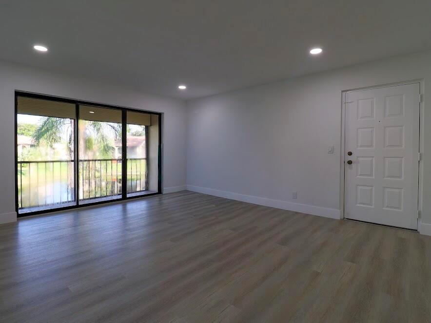 An empty living room features light wood-look flooring, recessed lighting, and a sliding glass door — 614 Sea Pine Way # H2, FL 33415, FL