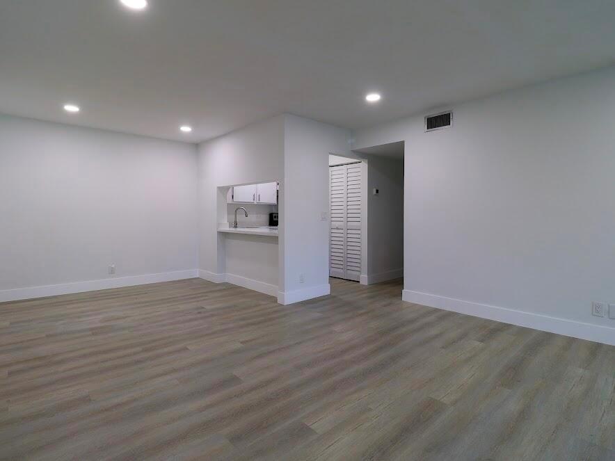 An empty living room features light wood-look flooring, recessed lighting, and a kitchen pass-through window — 614 Sea Pine Way # H2, FL 33415, FL