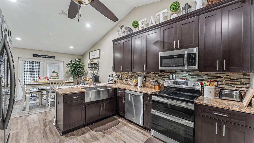 A kitchen features dark wood cabinets, stainless steel appliances, granite countertops, and a farmhouse sink — 1411 ASHBURY COURT, LAKELAND, FL