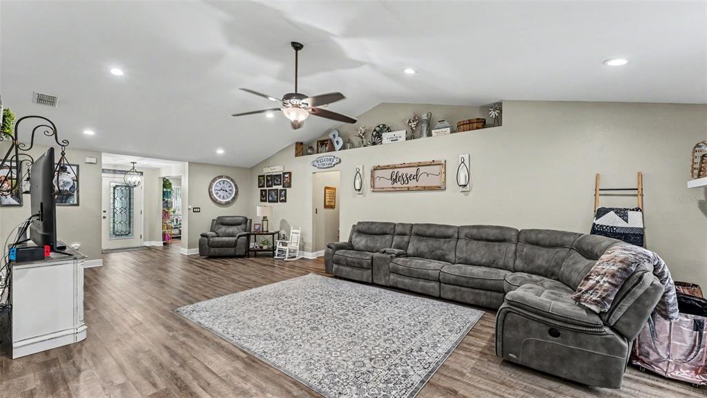 A spacious living room features a grey sectional sofa, wood-look flooring, and a vaulted ceiling — 1411 ASHBURY COURT, LAKELAND, FL