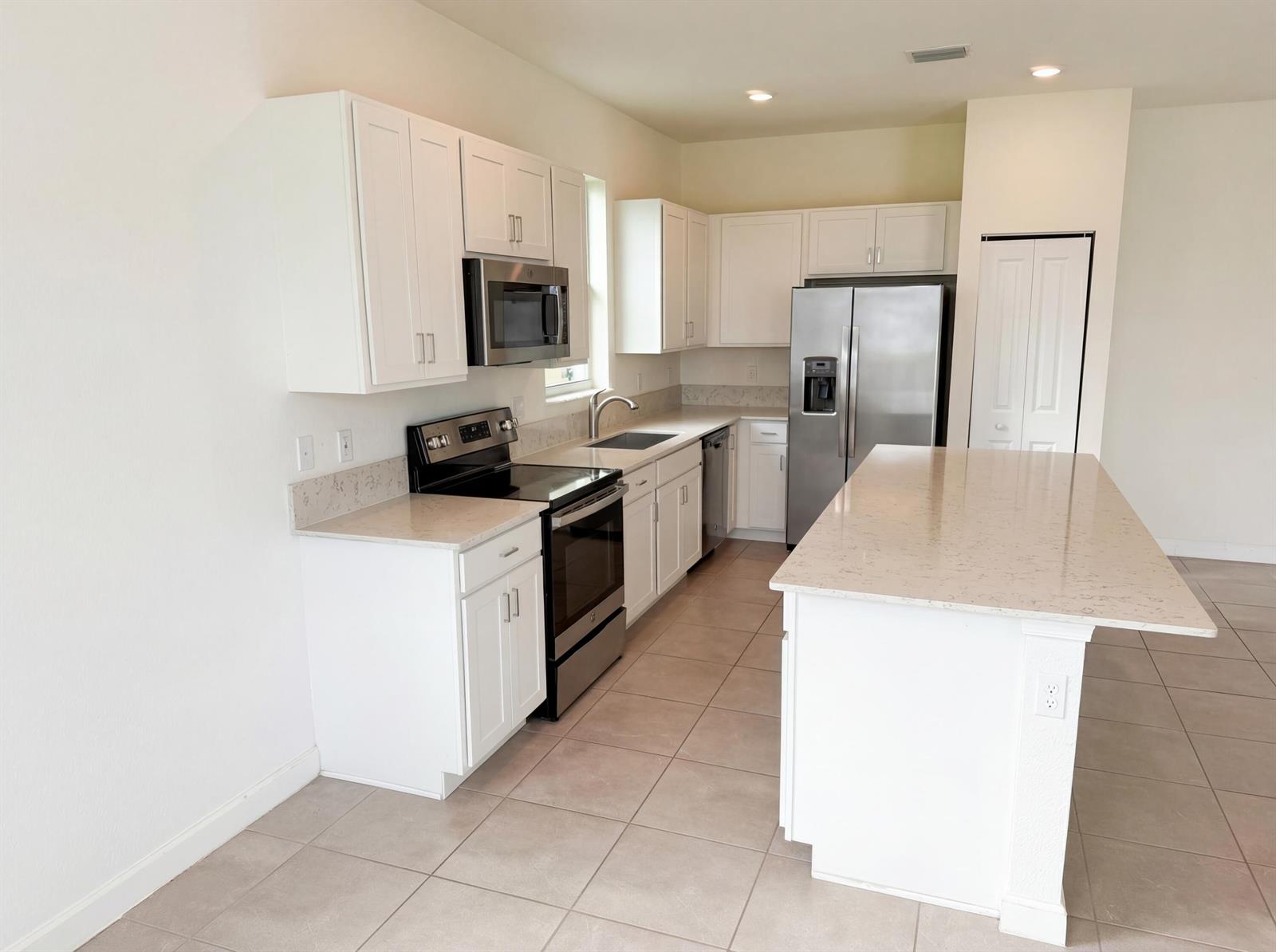 A kitchen features white cabinets, stainless steel appliances, a kitchen island, and light-colored countertops — 12473 NW Lynch Lane, FL 34987, FL