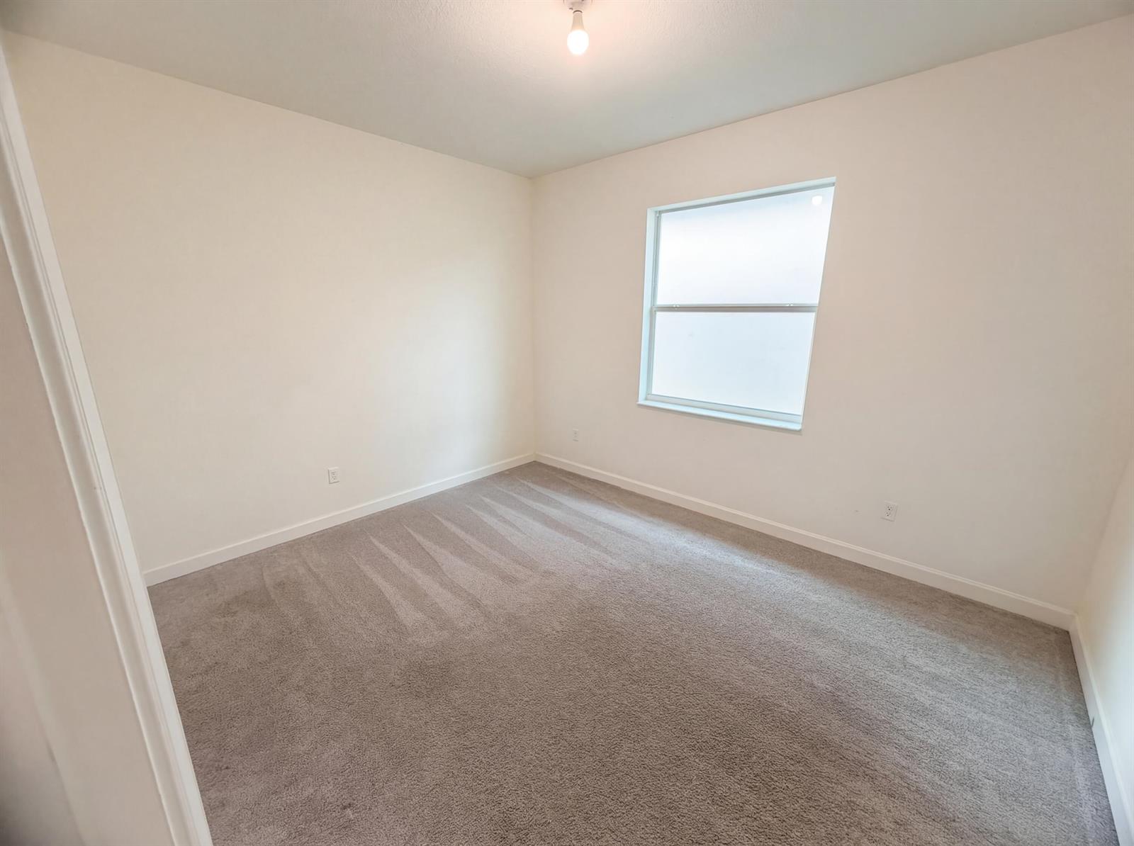 An empty bedroom features beige carpet, white walls, and a single window — 12473 NW Lynch Lane, FL 34987, FL