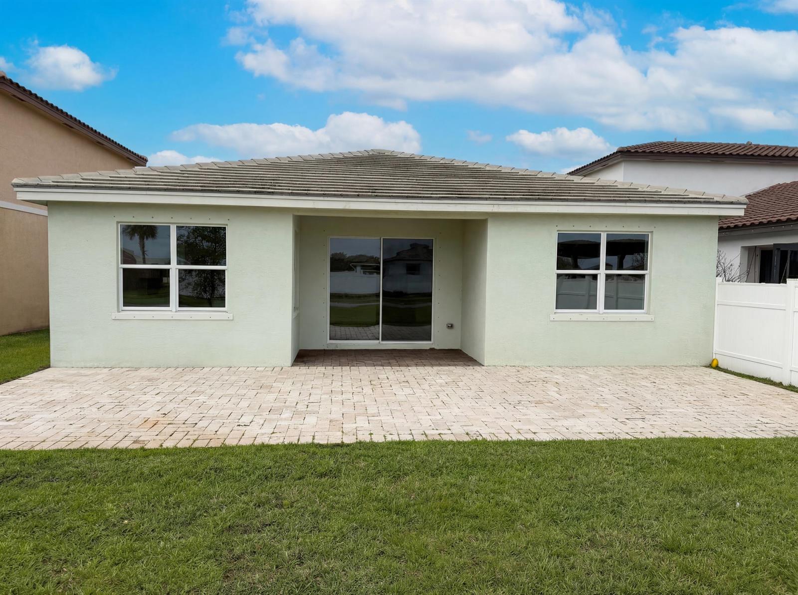 The back exterior of a light green house features a paved patio and sliding doors — 12473 NW Lynch Lane, FL 34987, FL